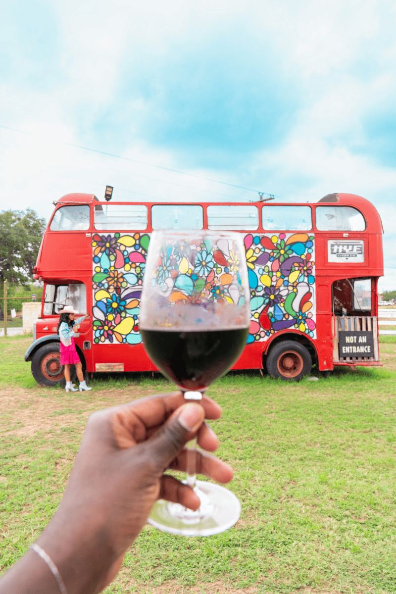 A person holding a wine glass in front of a red double decker bus with a woman 