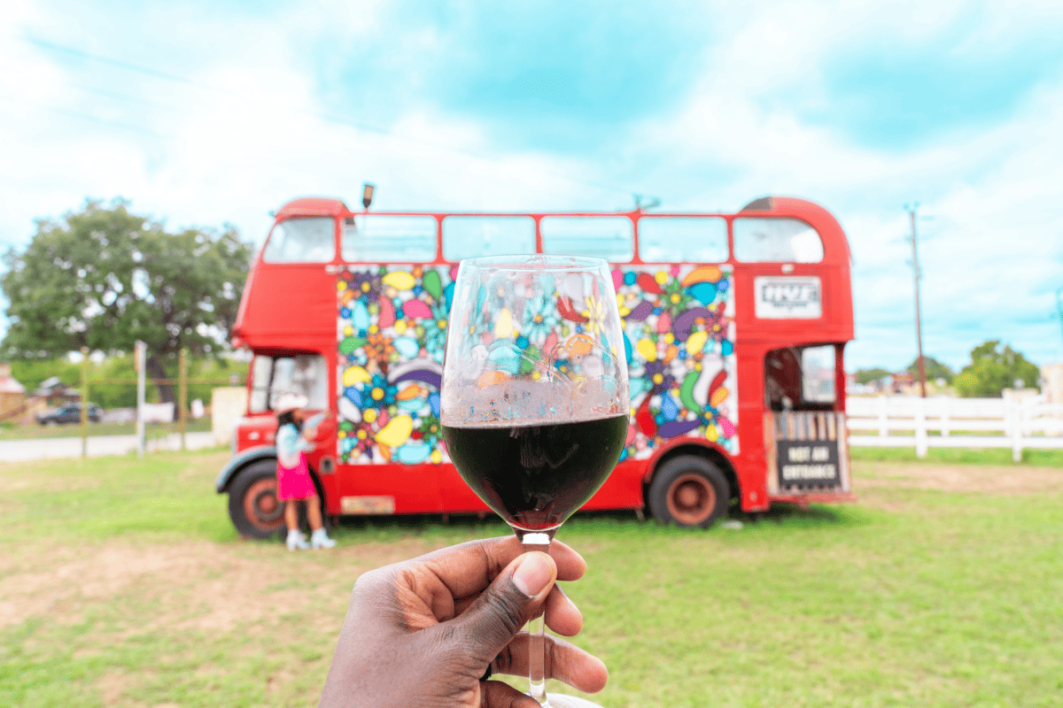 A person raising a glass of wine in front of a red bus