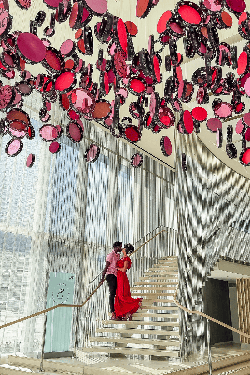 A couple kissing on a beutiful staircase of a hotel with red hanging decors on the ceiling
