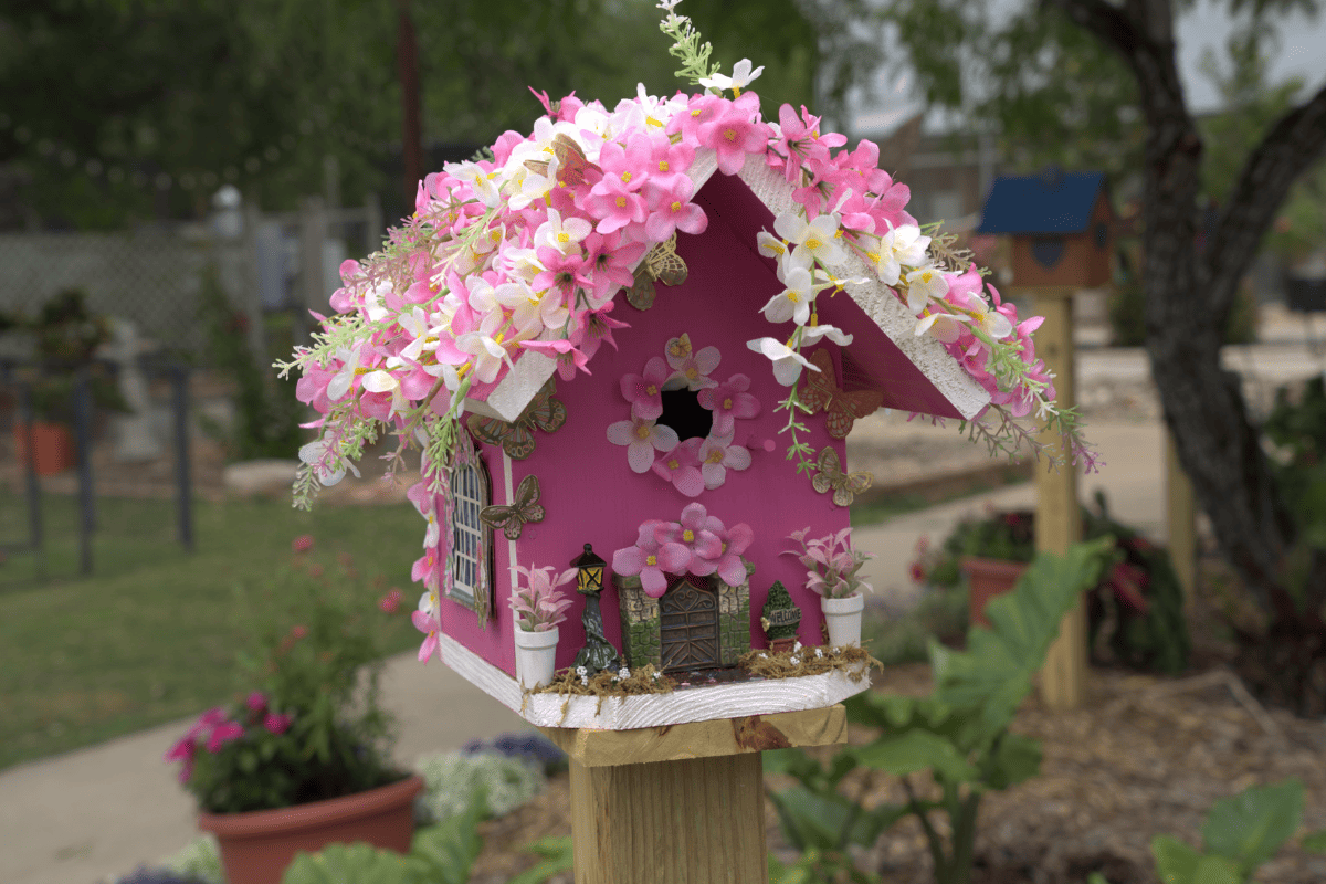 A cute pin bird house decorated with real small flowers.