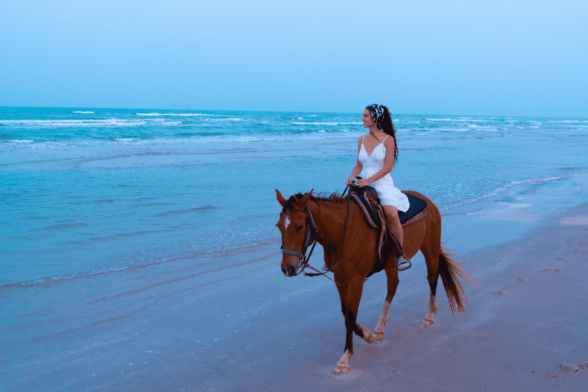 A woman in white dress riding on a horse along the beach