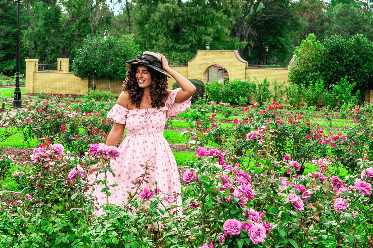 A woman in pink dress happily strolling on a rose garden 