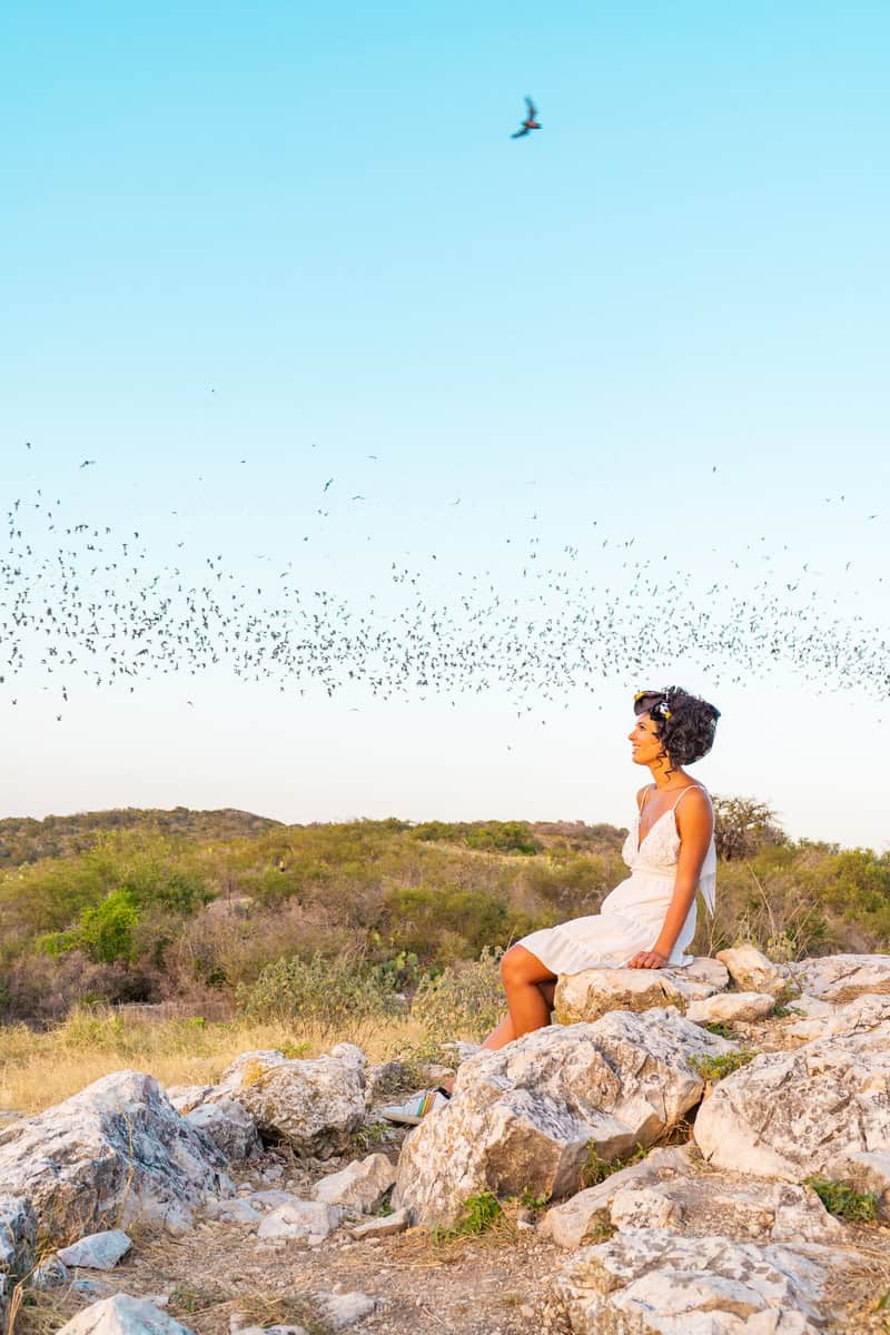 Jessica sits on a rock as birds fly overhead