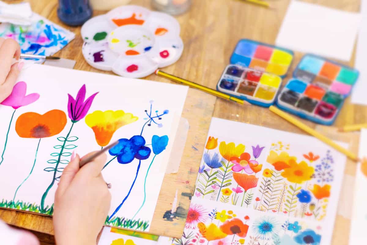 An artist painting flowers on paper with watercolor paints