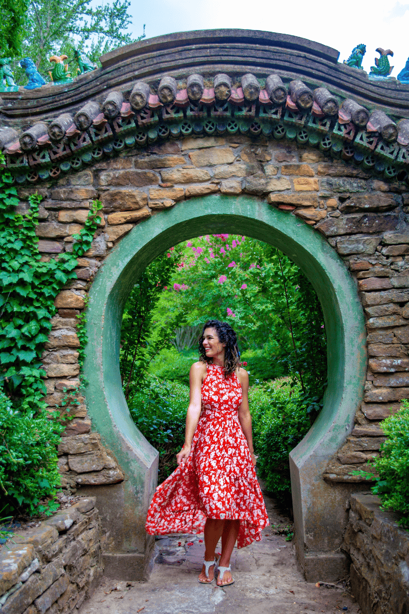 Jessica in a floral red dress twirls playfully under a stone archway