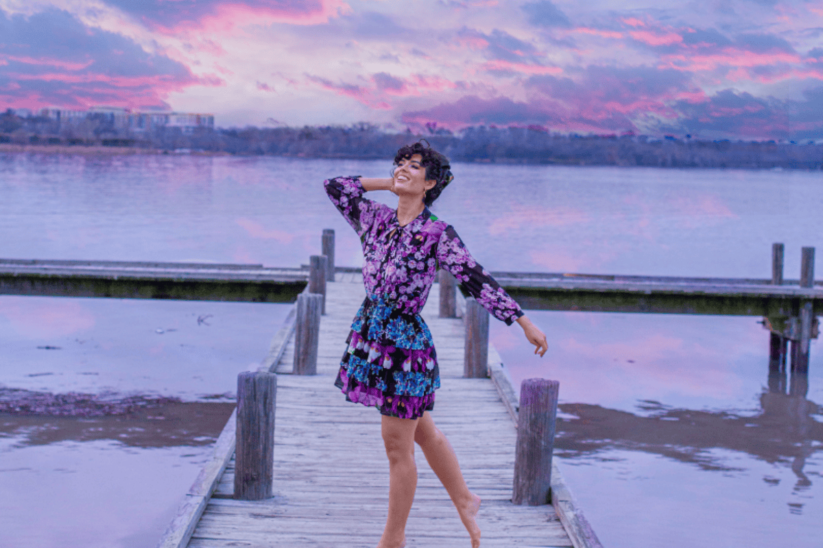 A person in a floral dress dancing on a wooden pier