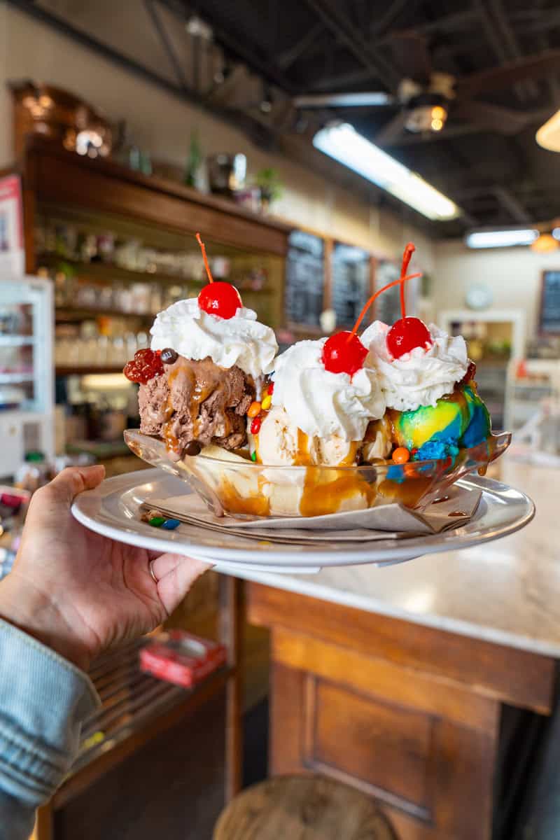 a hand holding a plate of ice cream sundaes