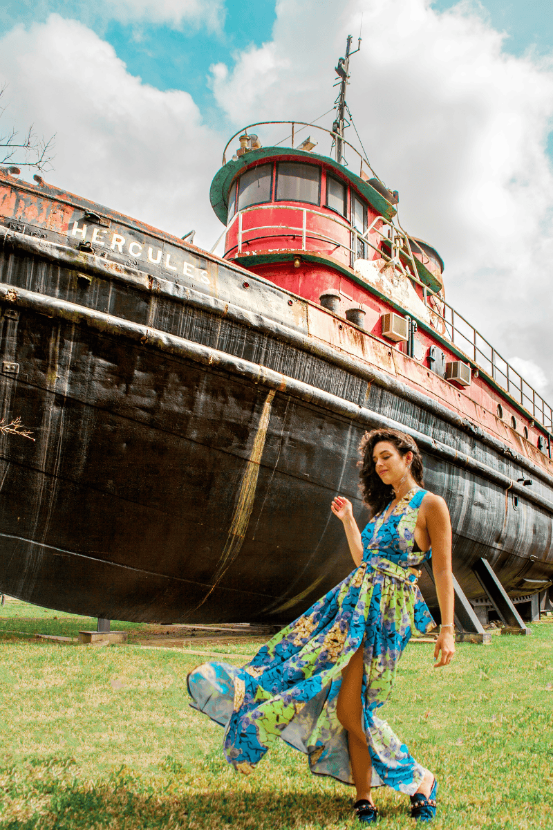 A lady in a flowing dress poses elegantly in front of a boat 