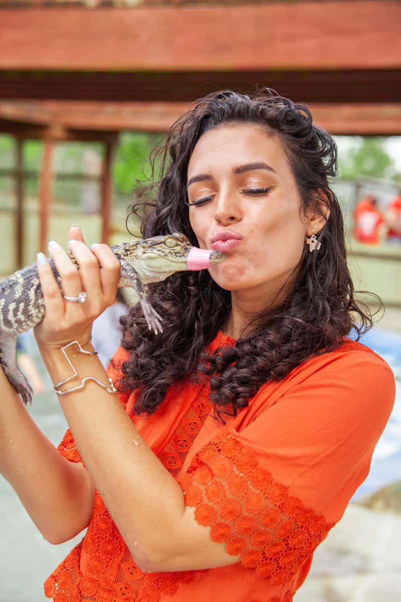 Woman in orange shirt kissing a lizard in a zoo