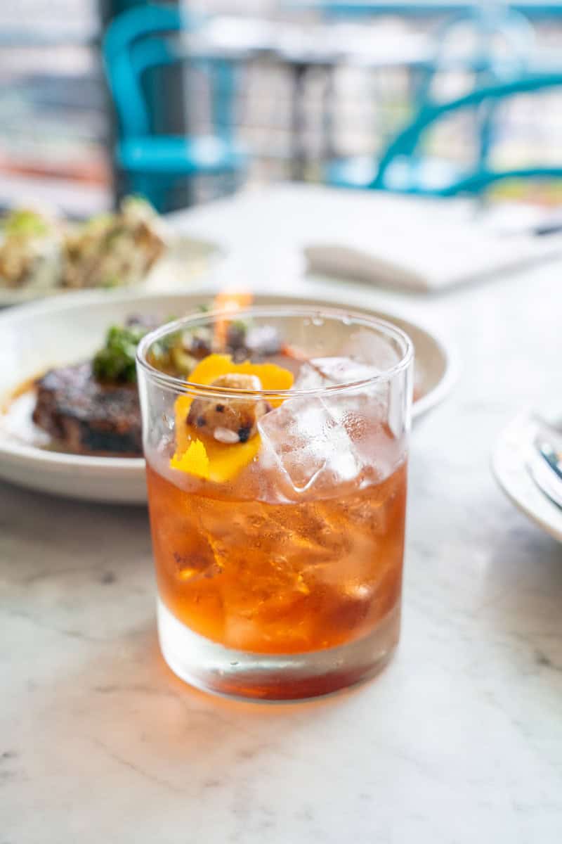 a glass of brown liquid with ice and orange slice on top