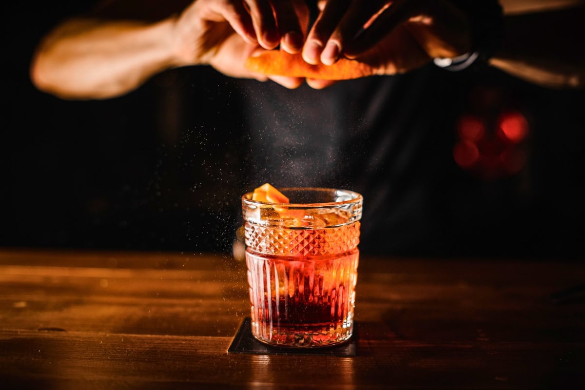 a person squeezing an orange into a glass of alcohol