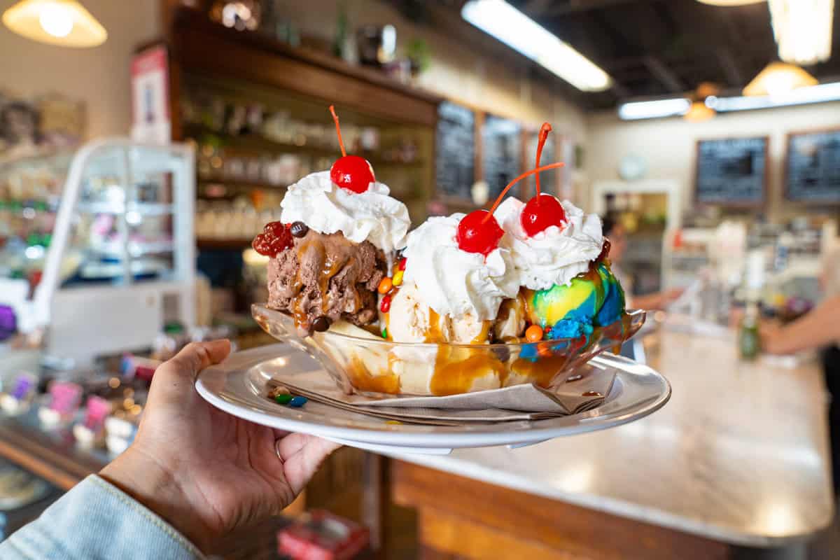 a hand holding a plate of ice cream sundaes