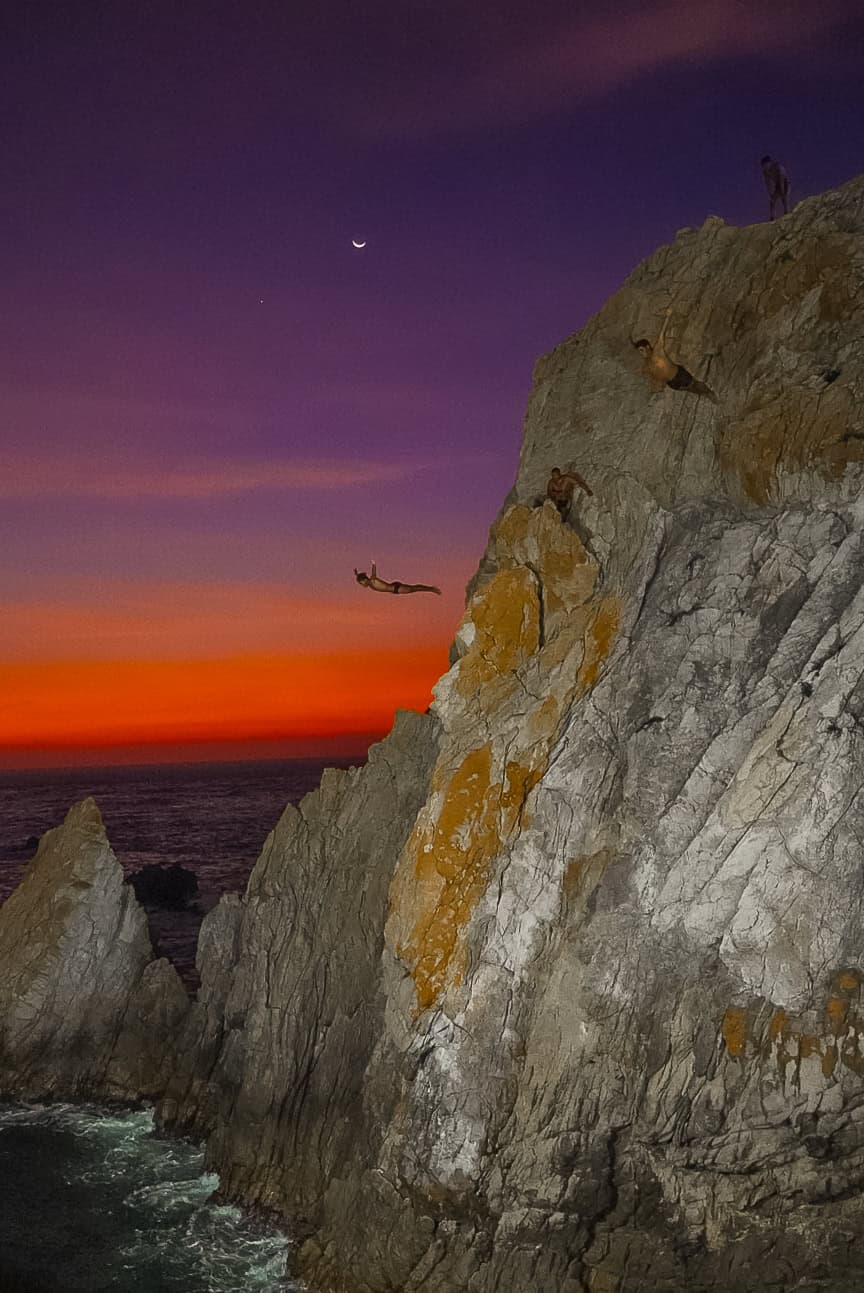 a rock cliff with birds flying over the water