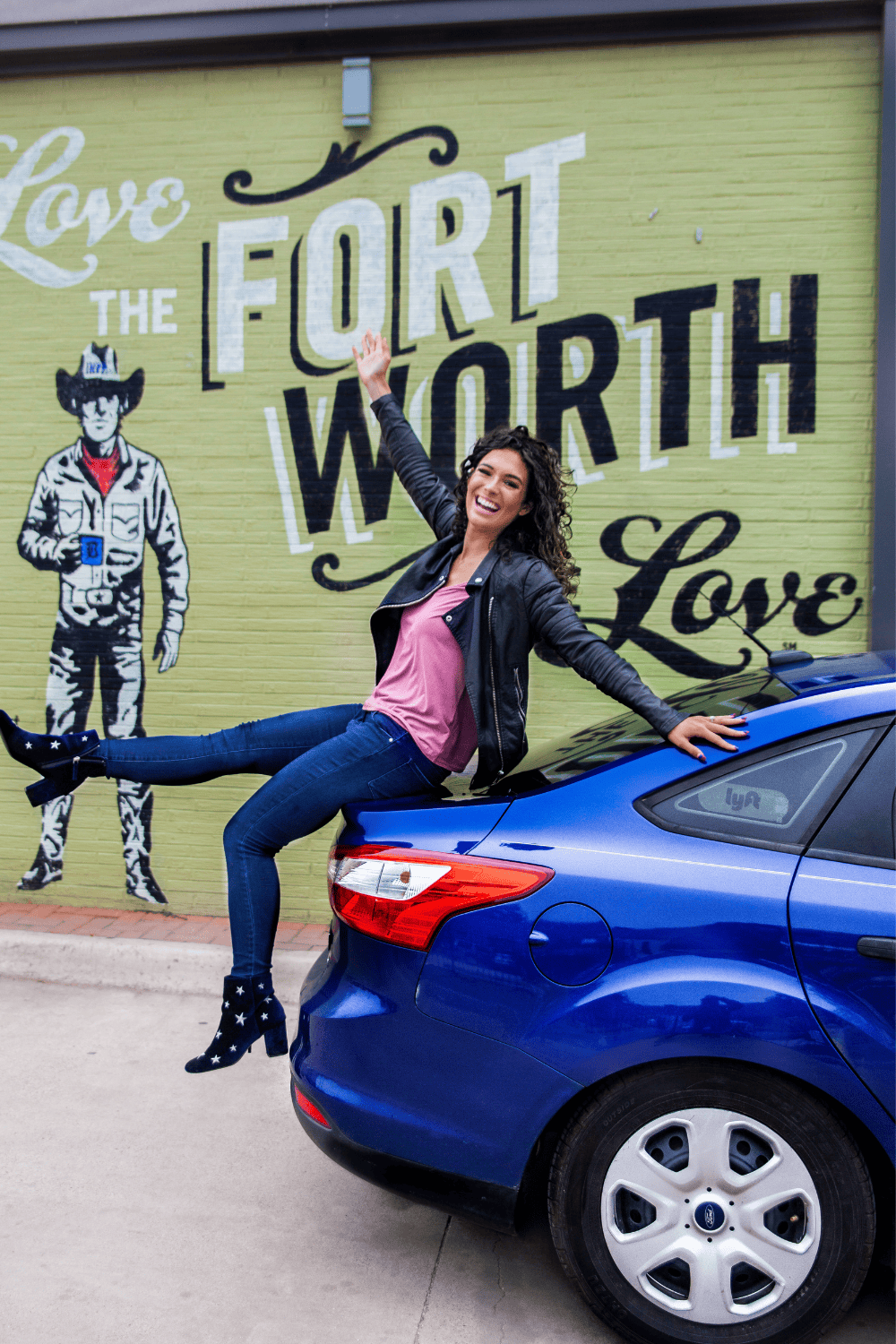 A woman sitting on the hood of a blue car