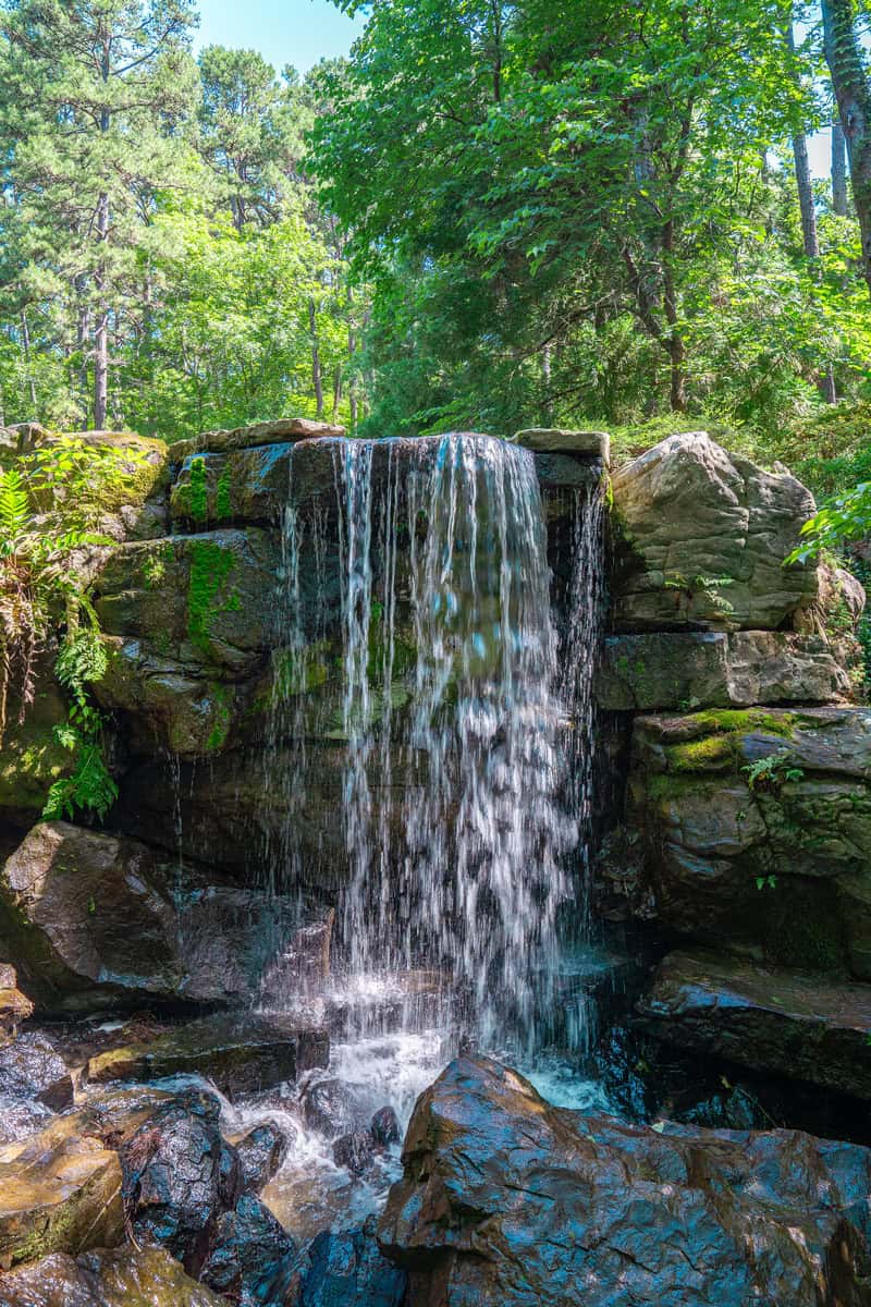 A serene waterfall flowing through a lush forest, surrounded by tall trees and vibrant greenery.