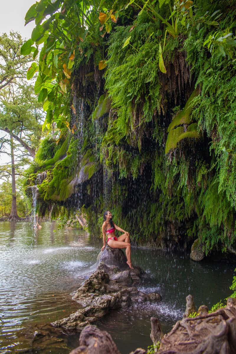 A woman enjoying the serene beauty of a waterfall, sitting peacefully on a rock.