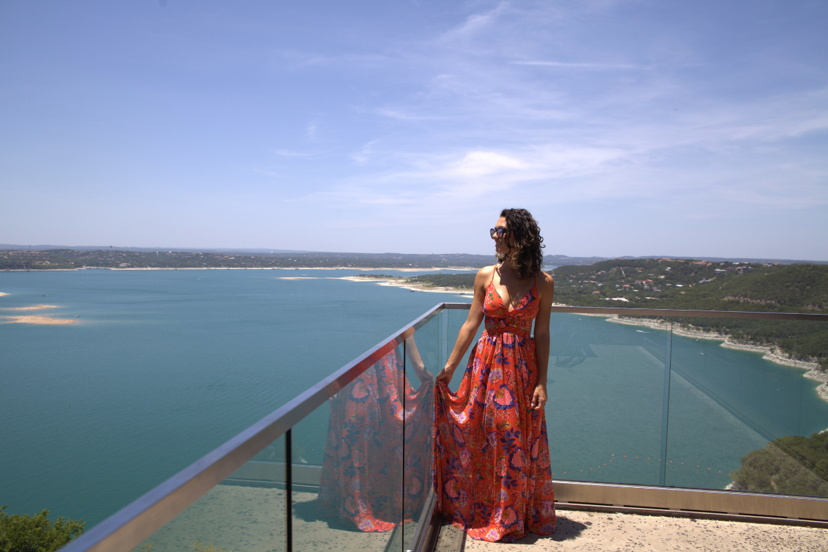  Woman in vibrant dress on balcony with lake view.