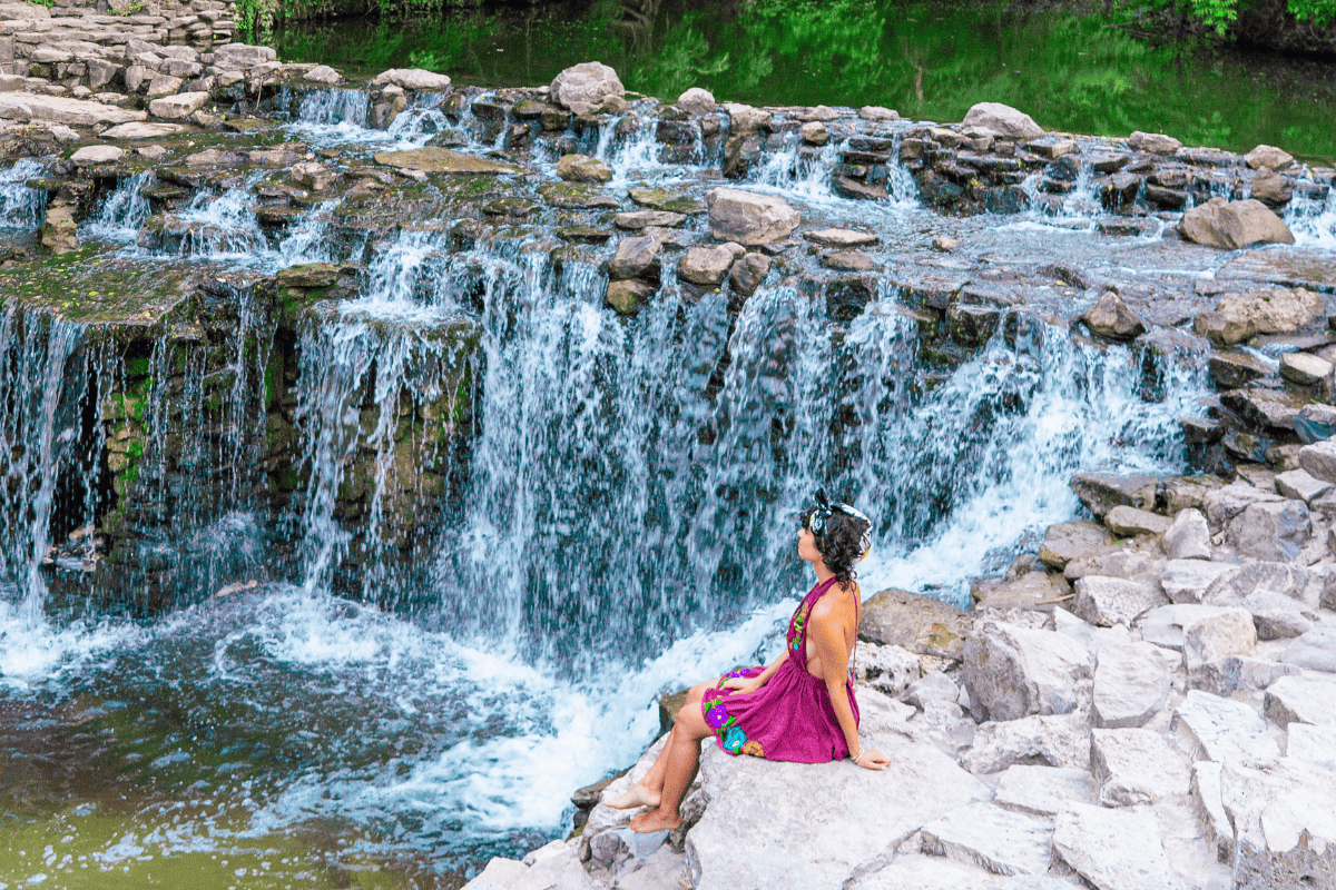 Woman sitting on rock near waterfall, enjoying nature's beauty.