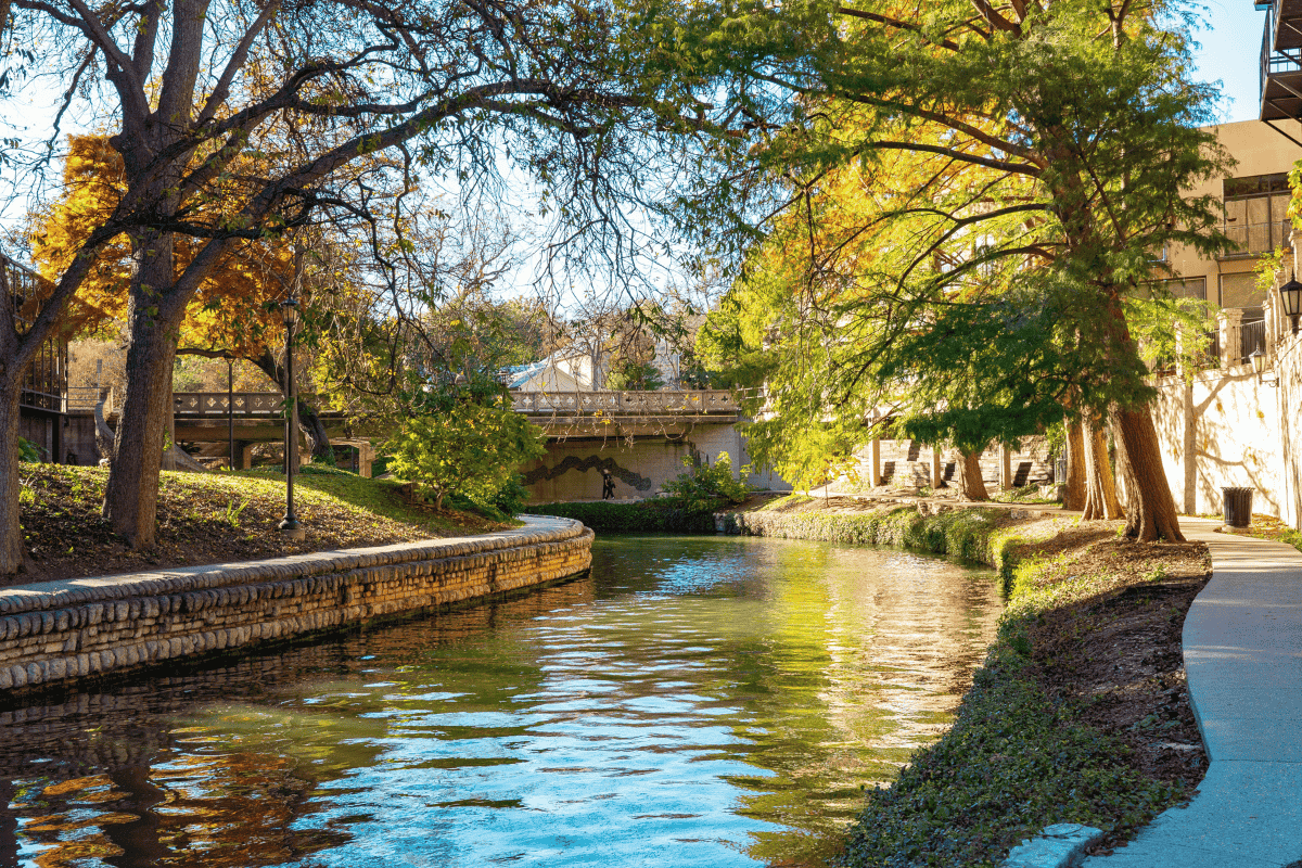 A scenic city river walk with lush trees and buildings lining the waterway.