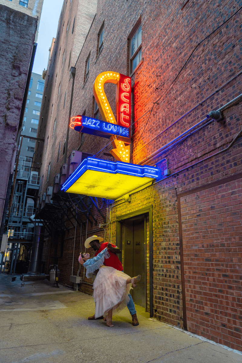 A romantic couple dancing gracefully in front of a neon sign.