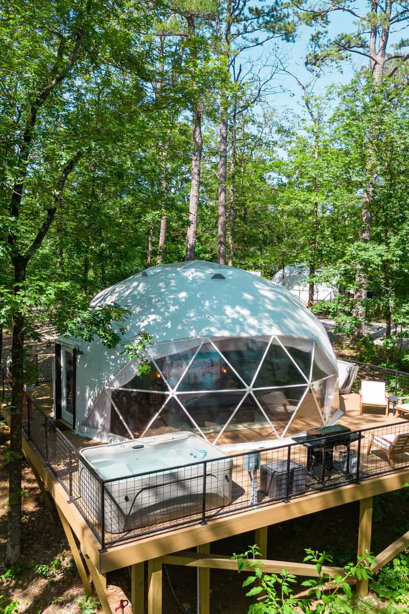 A cozy dome tent surrounded by lush greenery in the woods.