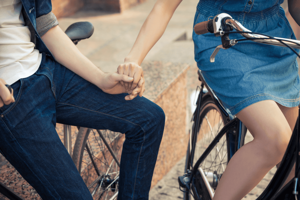 Romantic image of a couple on a bicycle holding hands.