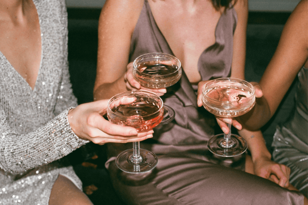 Three women in elegant dresses, toasting with champagne glasses in hand.