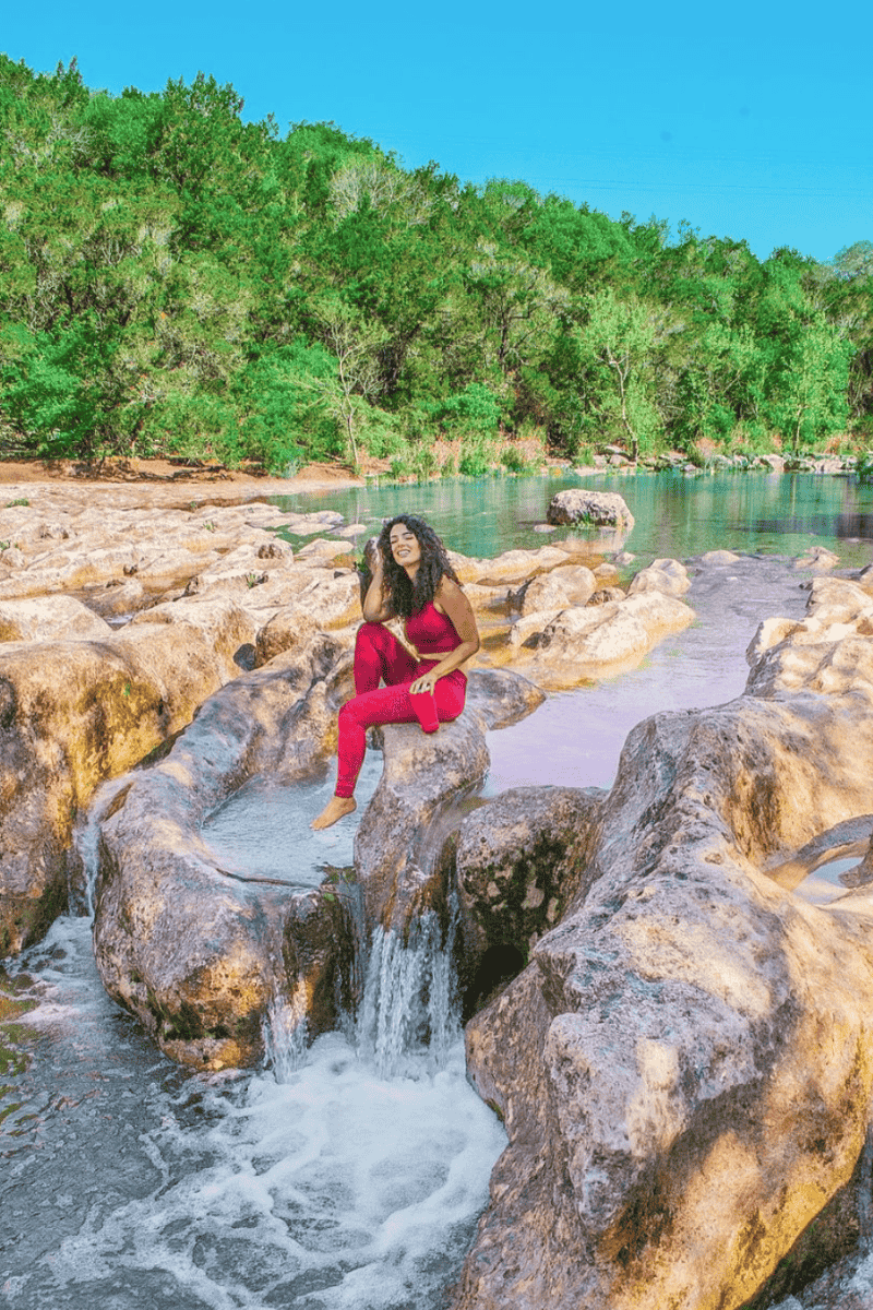 a woman sitting on rocks by a river