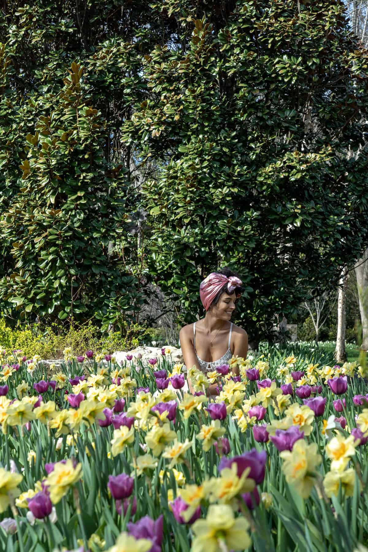 A person sits among vibrant yellow daffodils and purple tulips