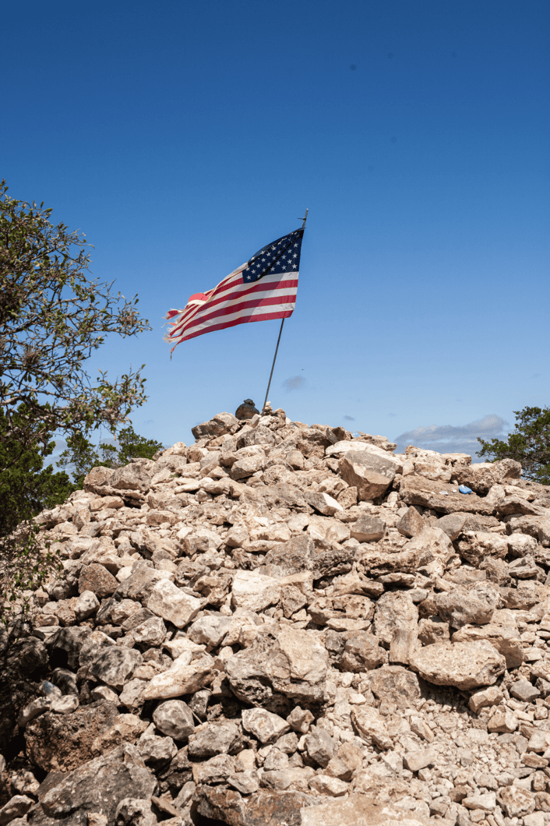 U.S. flag atop a rocky mound against a blue sky.