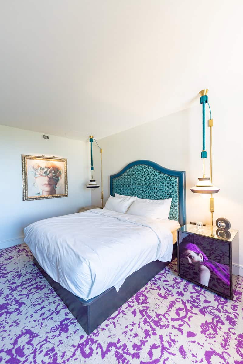 Bedroom with purple and white carpet, bed with cozy blankets and pillows.