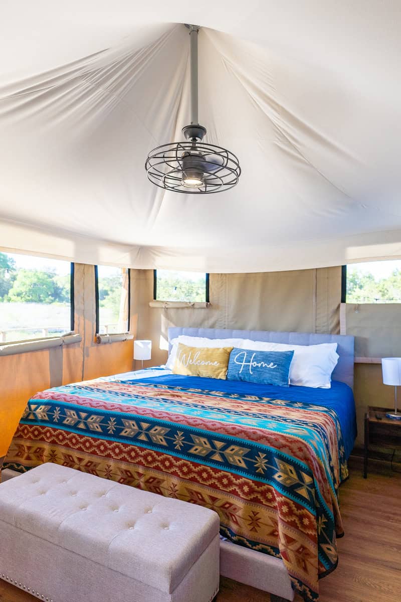 Cozy bed inside a tent with a ceiling fan above.