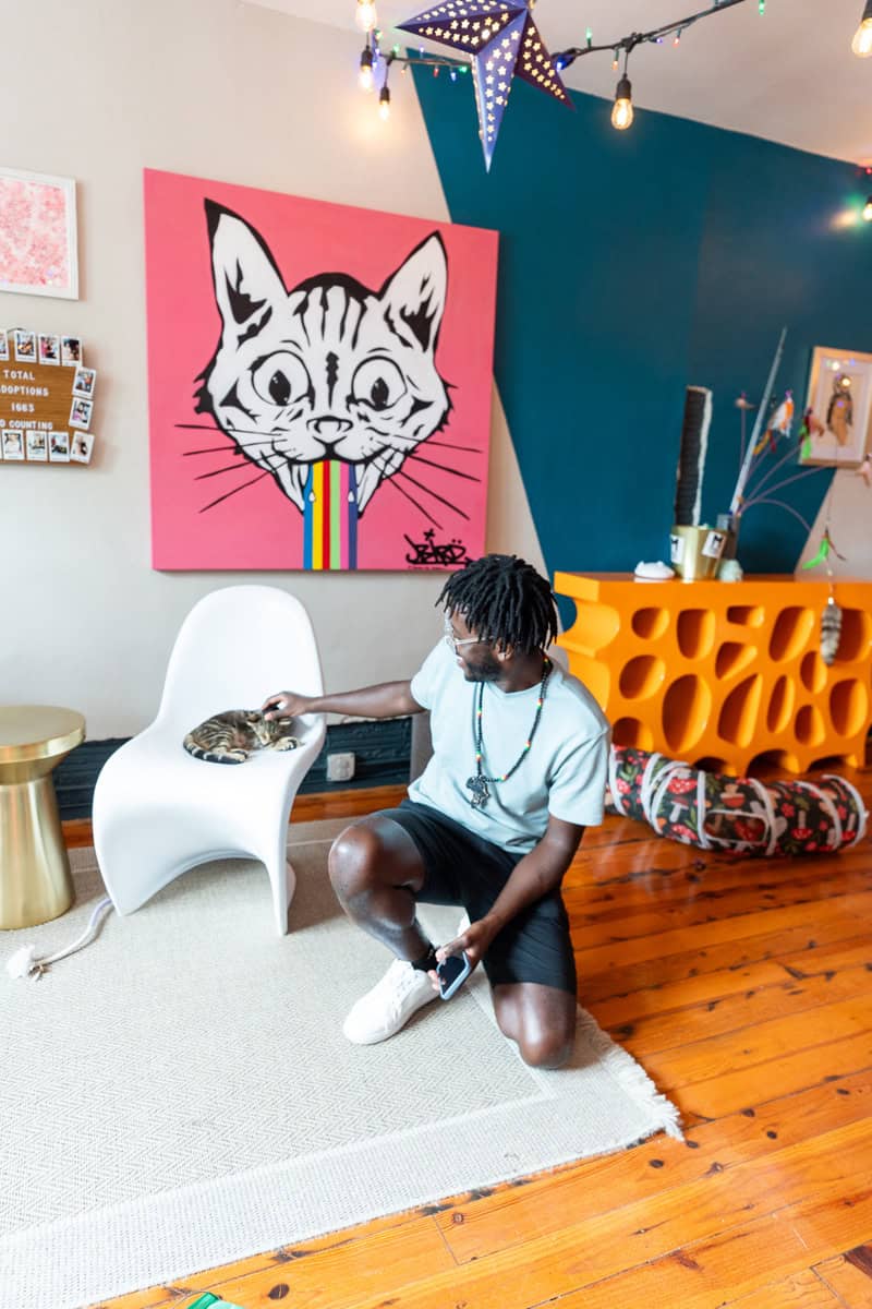 a man kneeling on the floor with a cat on a chair