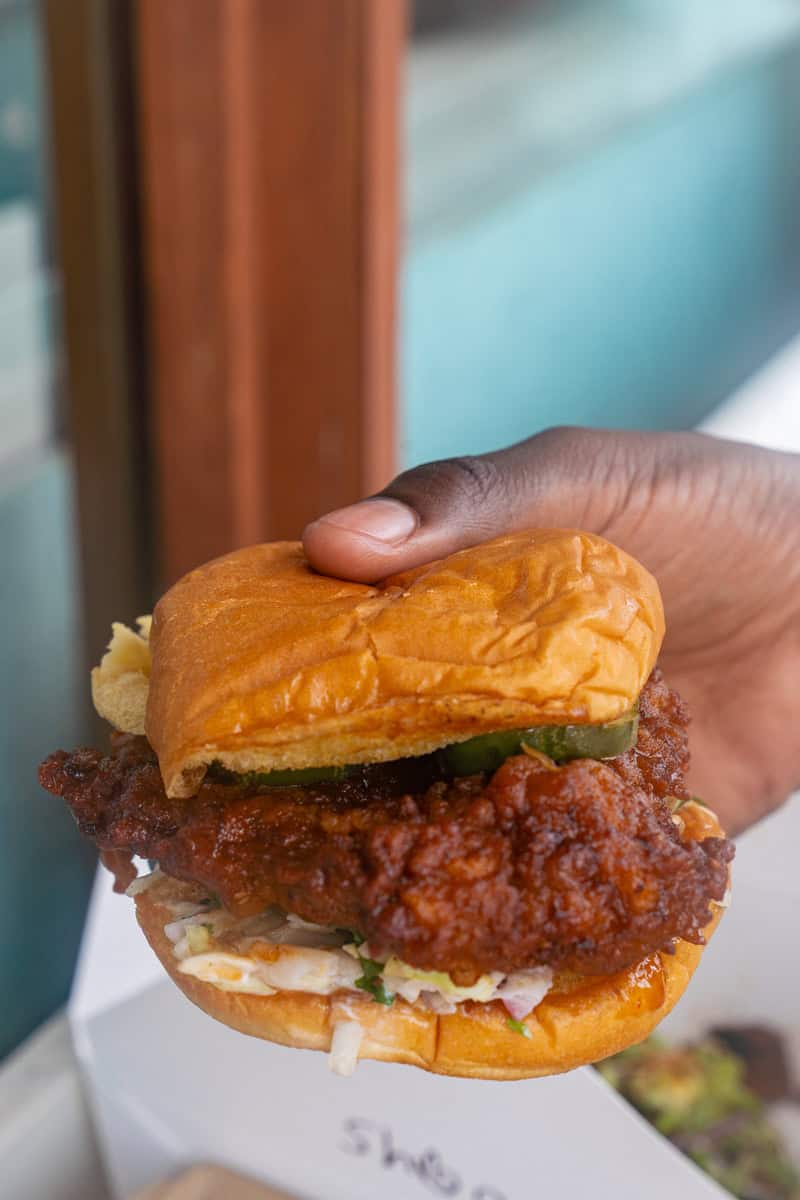 Person holding a sandwich with a pickle on top.