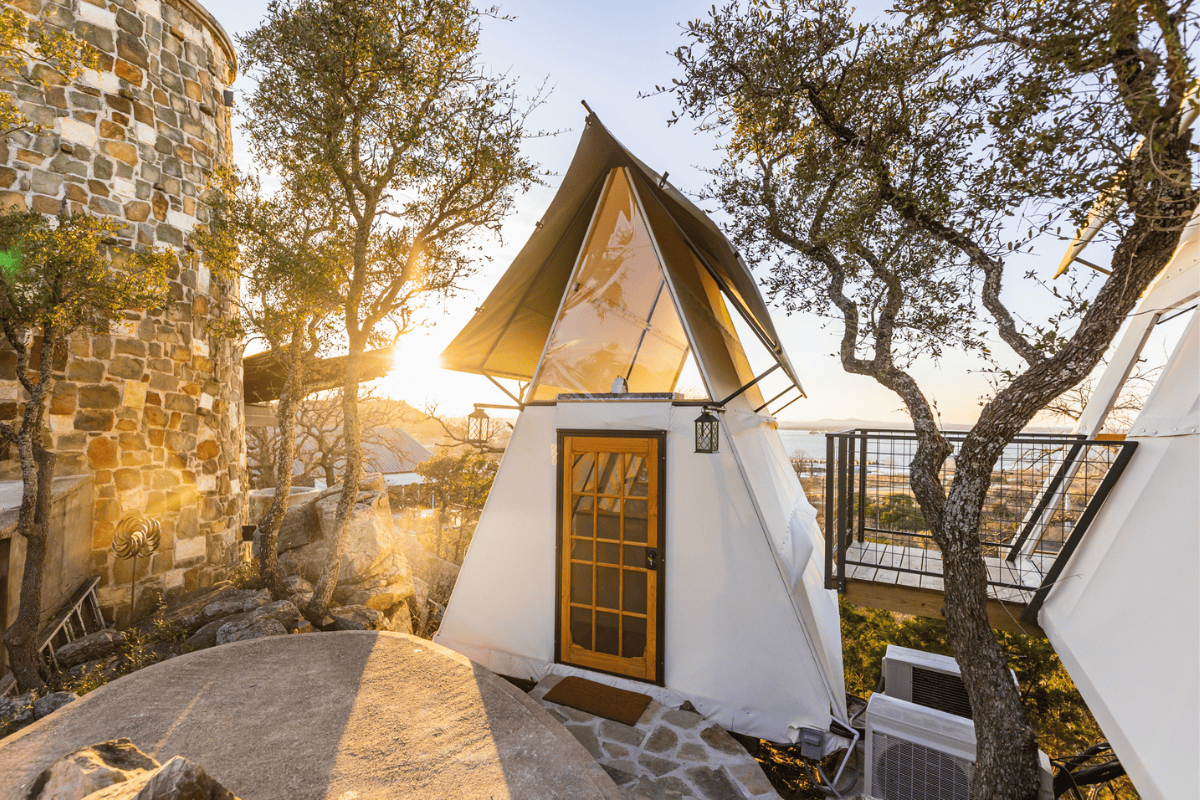 Glamping tent and stone tower in a serene setting with trees at sunset.