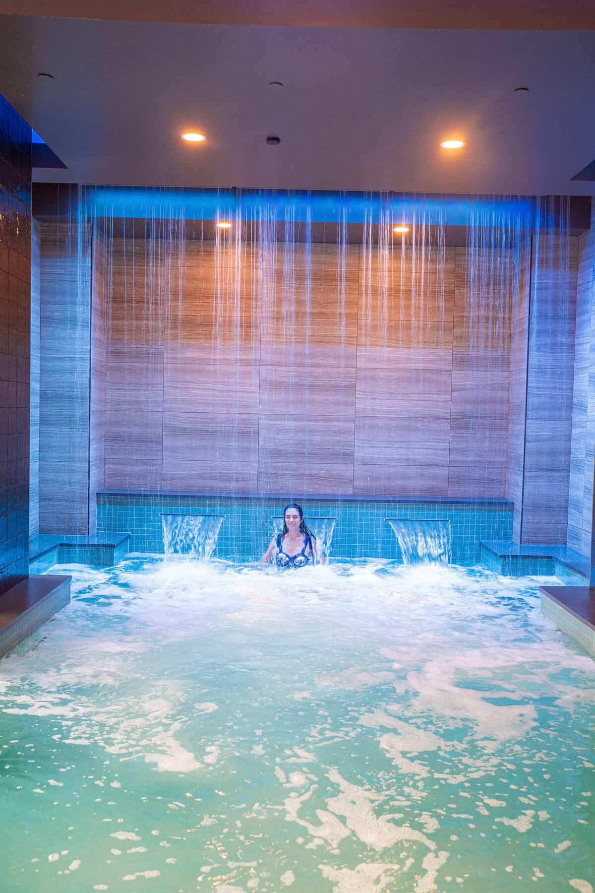 a woman in a pool with water falling from the ceiling