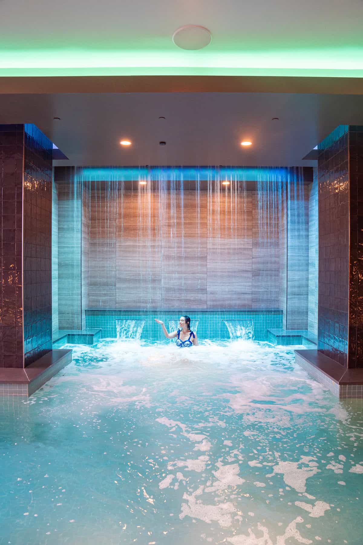 a woman in a pool with water falling from the ceiling