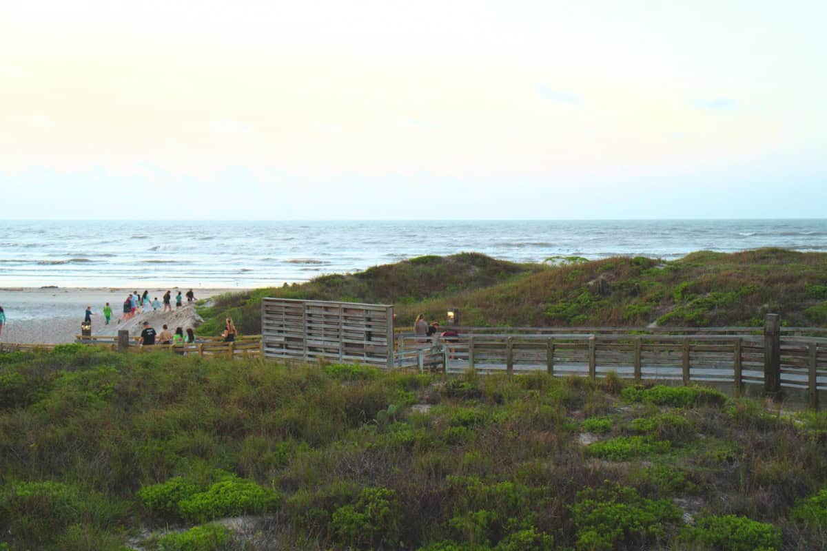 People gather on a coastal boardwalk overlooking a serene beach at dusk.