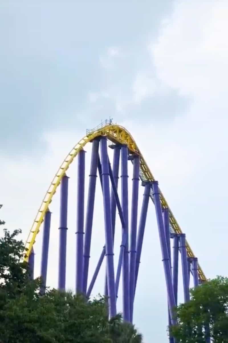 A towering purple roller coaster with yellow rails against a blue sky.