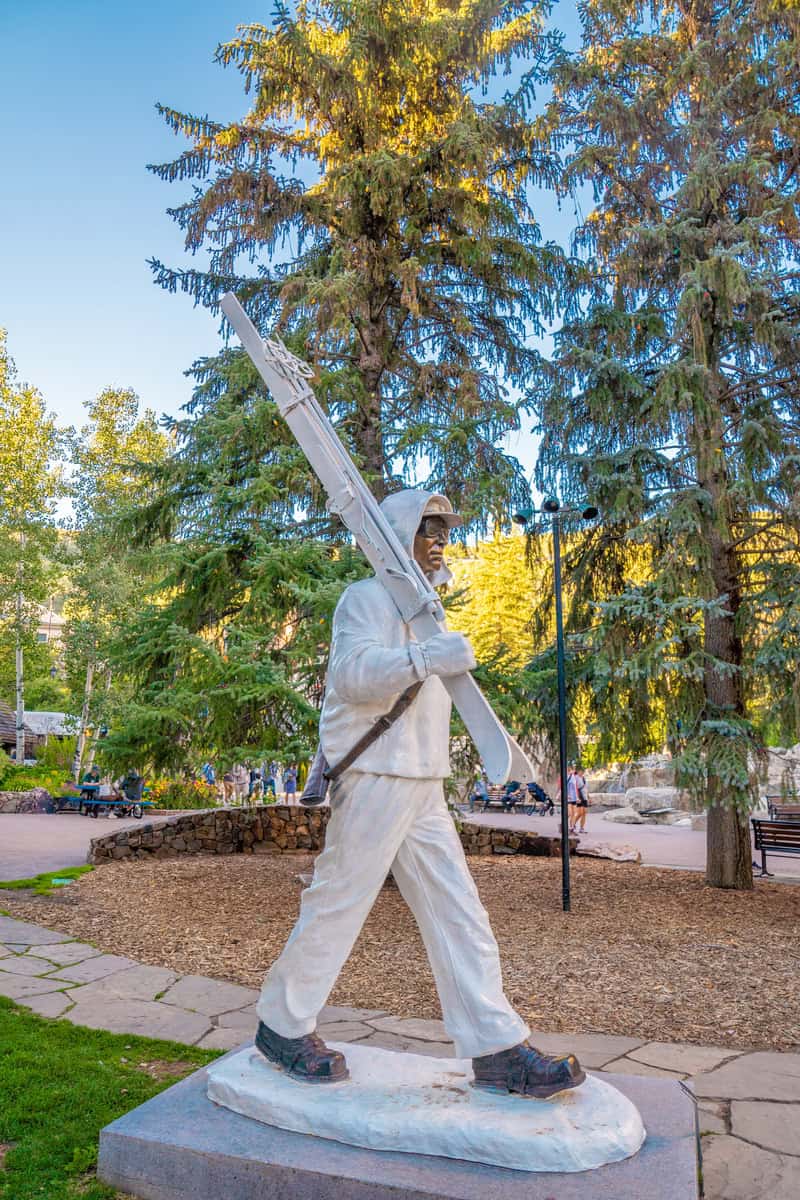 Statue of a person carrying a large ski, set in a park