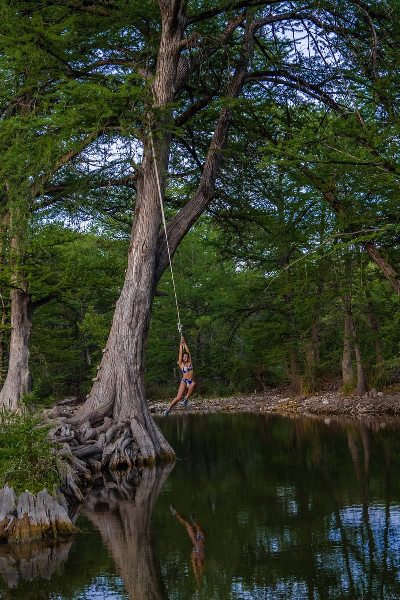 Person on a rope swing hanging from a tree over river water