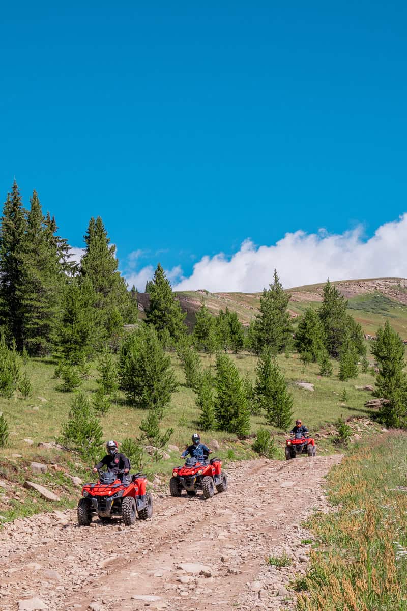 Three people riding ATVs on a rocky mountain trail