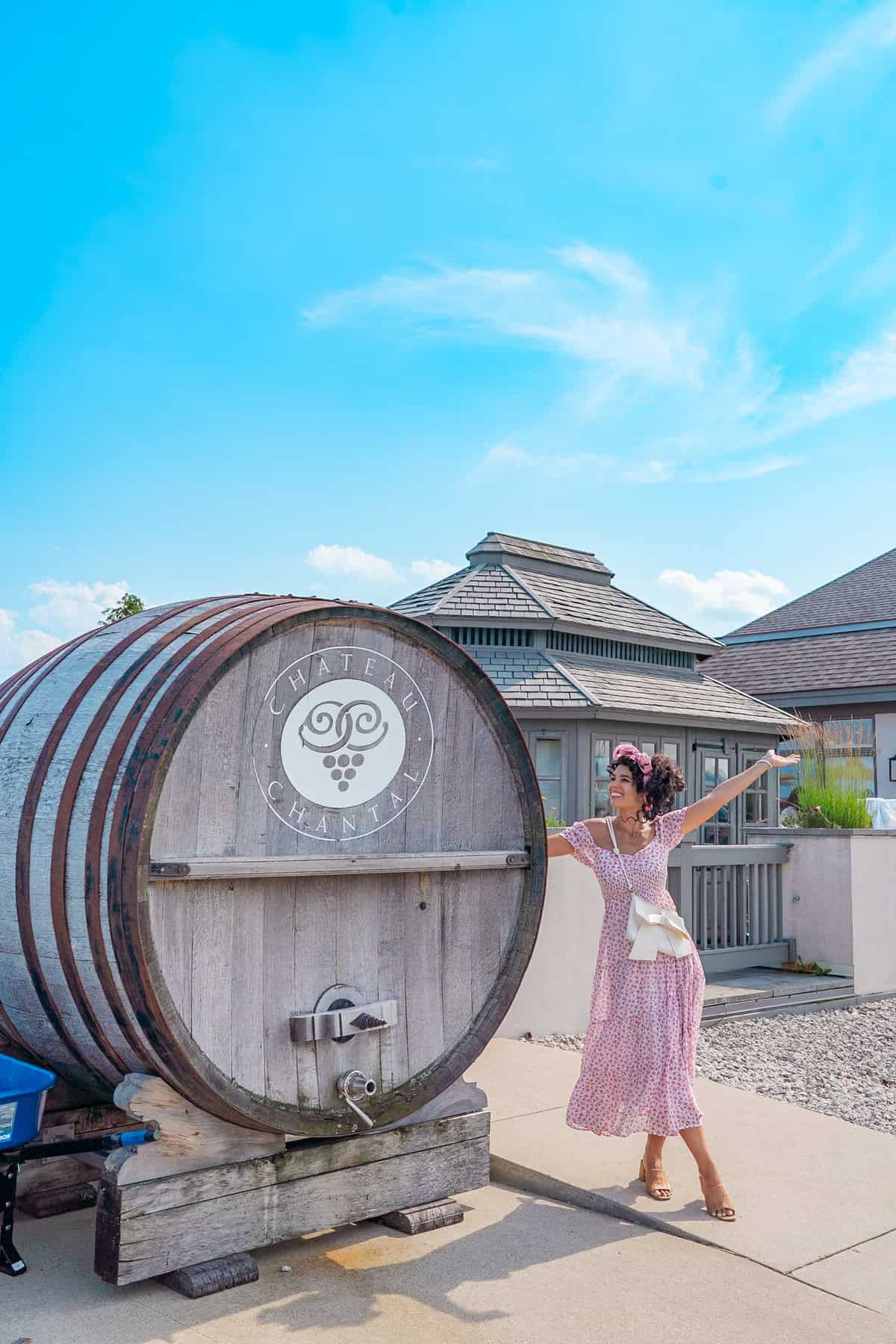 Person in pink dress posing next to a large wine barrel with "Chateau Chantal" logo under a blue sky.