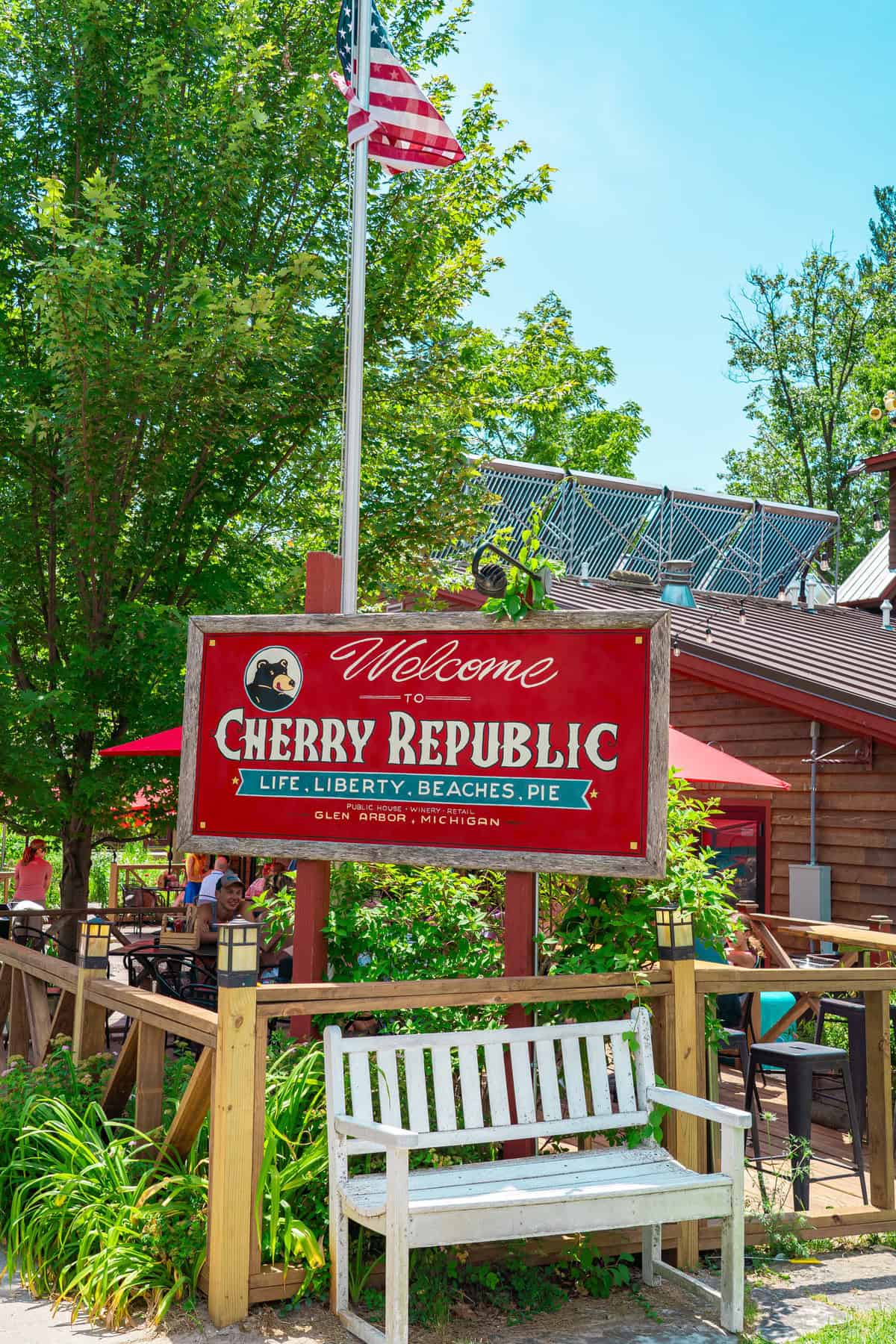 "Welcome sign to Cherry Republic with motto and US flag above a white bench."