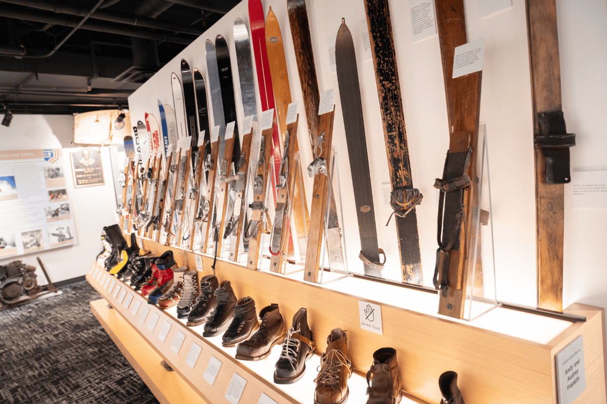 Vintage skis and boots displayed on a wall in a museum exhibit.