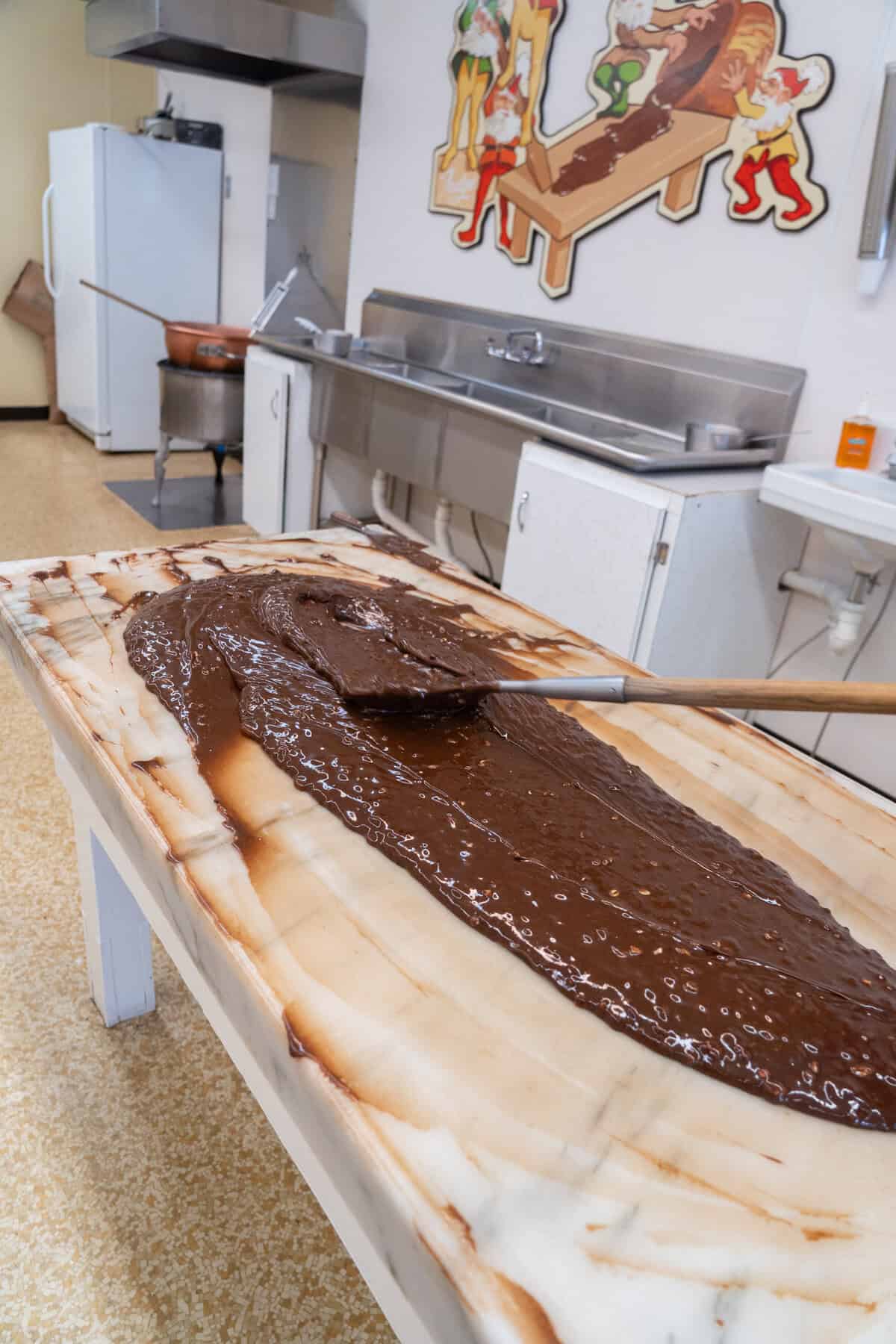 A chocolate spread being smoothed on a large marble slab in a confectionery kitchen.