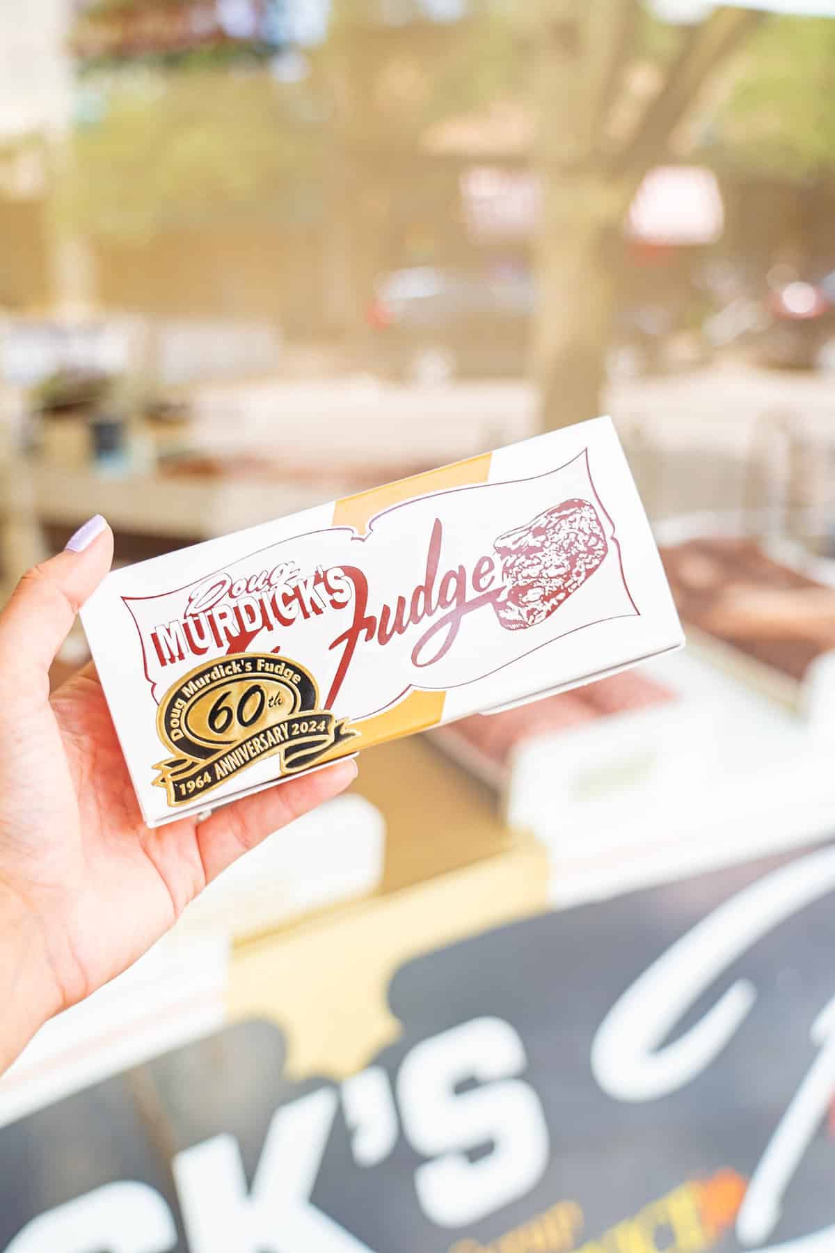 Hand holding a "Murick's Fudge" box with blurry background.