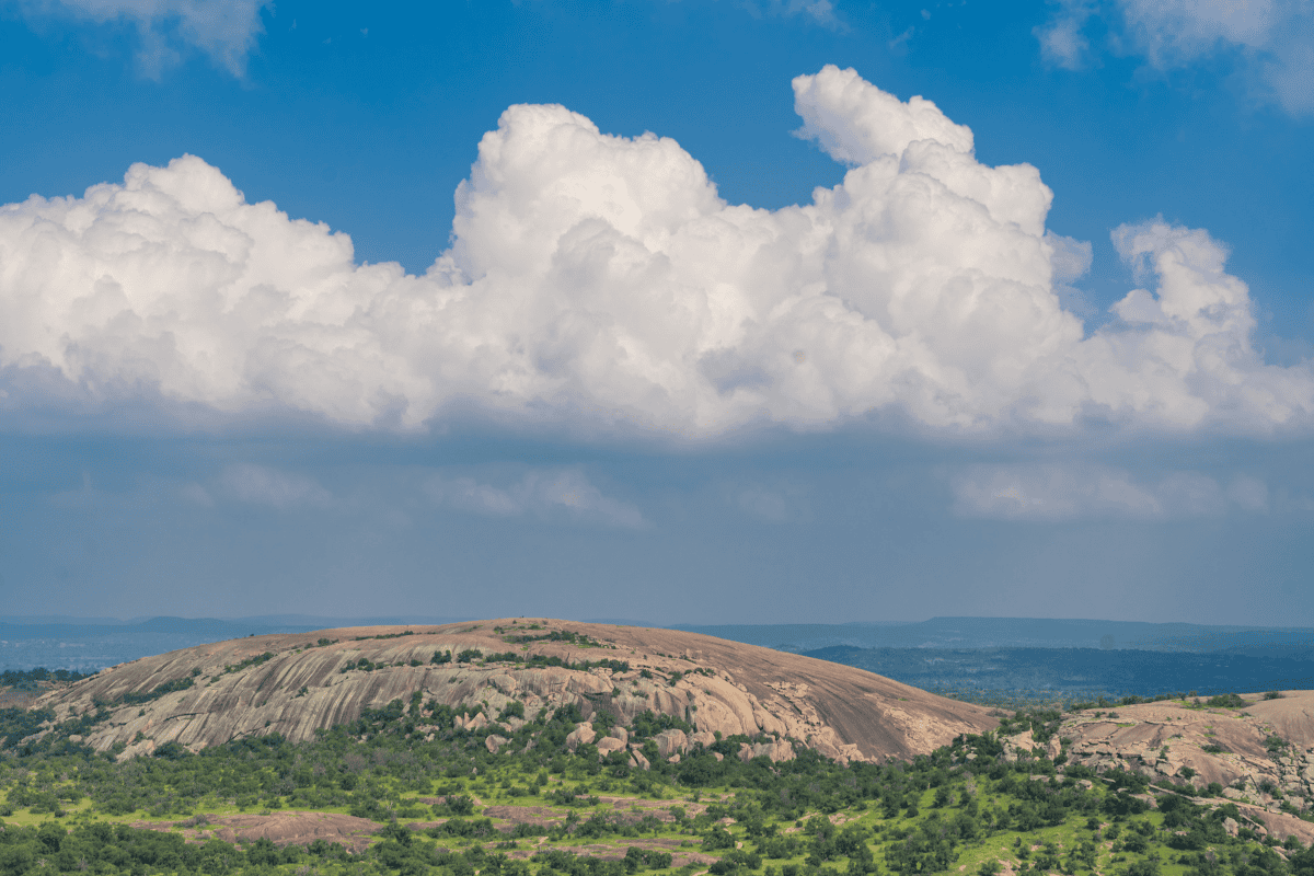 Vast blue sky with fluffy clouds over a smooth, domed hill