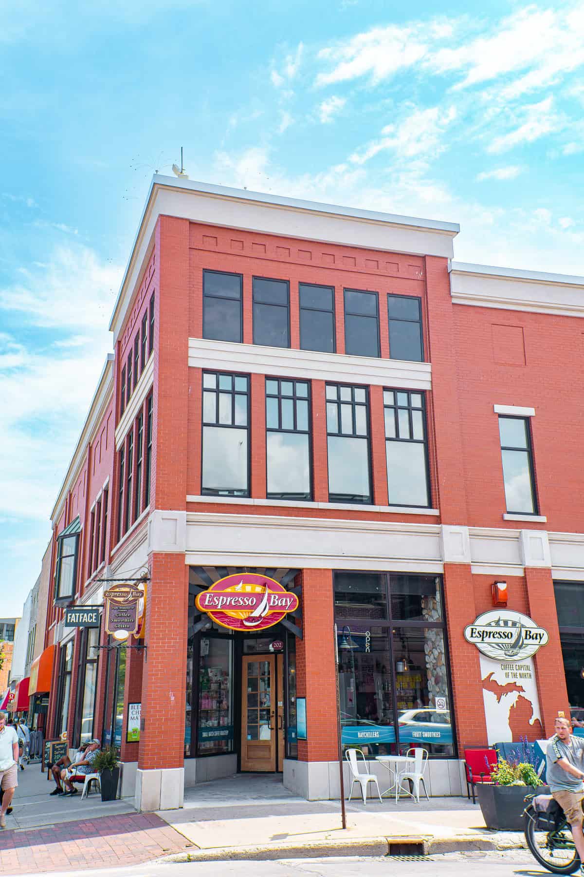 A red-brick corner building with "Espresso Bay" cafe on the ground floor and clear blue skies above.