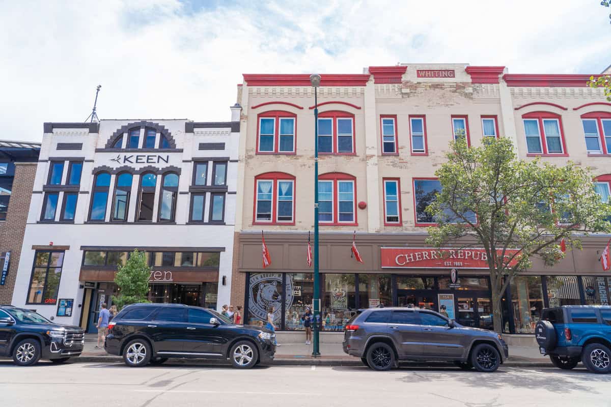 Street view of historic buildings with storefronts and parked cars.